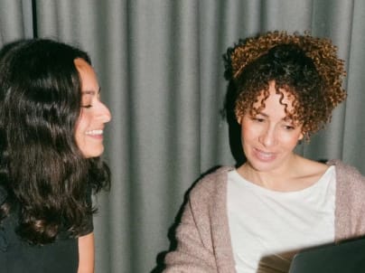 Two women sitting together, looking at a laptop screen and smiling.